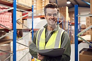 Male Worker Wearing High-Vis Vest Inside Busy Warehouse Checking Stock On Shelves Using Clipboard