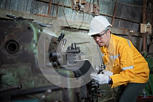 Male worker wearing yellow work clothes glasses white hardhat and wear glove inspecting the machine with tablet device.