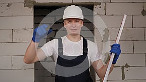 A male worker in a white helmet and overalls with a measuring construction tape.