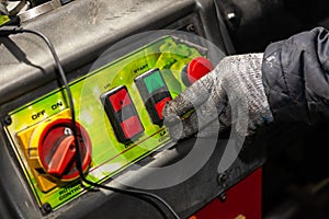 A male worker in working gloves presses the red button on the machine control panel in a workshop or factory. Industry and