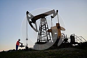 Male worker working with petroleum pump jack in oil field.