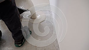 A male worker working with self-levelling cement mortar during a floor repair. A worker pours a bucket of mortar to