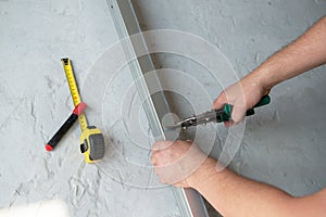 Male worker works with profile for drywall, cuts it with metal shears. Construction work, repair.