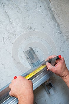 Male worker works with profile for drywall, marker marks for cutting. Construction work, repair.