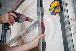 Male worker works with profile for drywall, setting, assembling with drill. Construction work, repair.