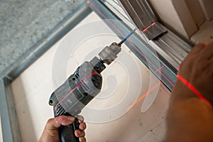 Male worker works with profile for drywall, setting, assembling with drill. Construction work, repair.