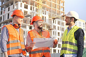 Male workers engineers at construction site in helmets hardhats near high-rise building skyscraper