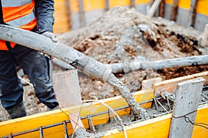 male workers pouring concrete with concrete hose. Details of construction site and close up details of worker workwear