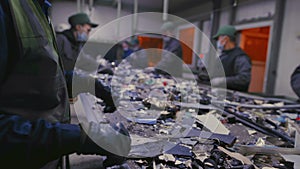 Male workers of a trash recycling plant sort through garbage on a conveyor belt. Garbage factory