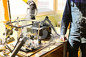 A male working electrician in a robe professionally works on a table for repair in a workshop for remoting electronics and