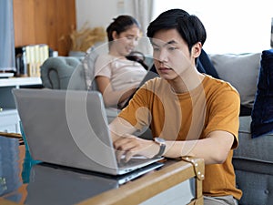 Male working at home with laptop on coffee table while female relaxed lying on sofa in living room