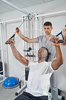 Male working out at gym supervised by physiotherapist