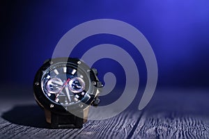 Male wrist watch on table under light beam over dark blue background