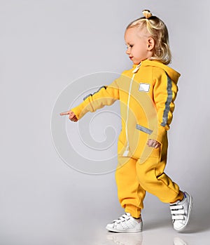 Little cute blonde girl in a warm comfortable overalls standing against a gray wall. Happy childhood and fashionable photo