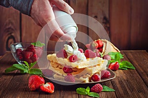 Males hand putting whipped cream on belgian waffle