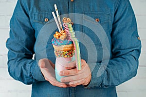 Males hands holding freak shake topping with donut, popcorn and