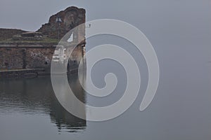 Mallards swimming next to an ancient pier of a lake on a foggy day in an italian town