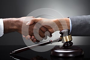 Mallet And Gavel In Front Of Two Businesspeople Shaking Hands