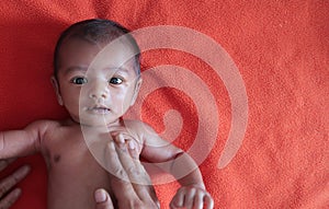 Malnourished baby looking at the camera lying on orange red velvet cloth background. protein energy malnutrition concept