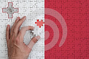 Malta flag is depicted on a puzzle, which the man`s hand completes to fold