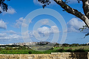 Malta landscape buildings in Qawra, with blue sky and white clouds and stone wall