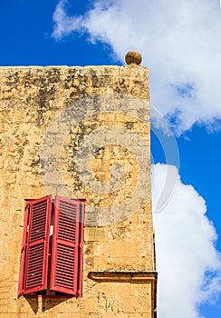 Malta, Mdina. Red window on a yellow sandstone wall in the old medieval city. Blue sky background