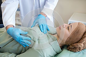 Mammologist in blue protective gloves palping breast of his patient