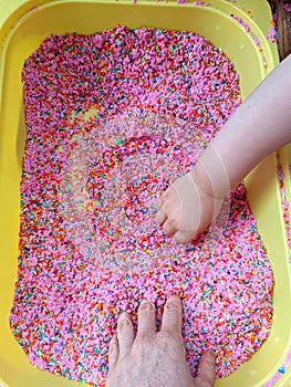 Mammy mother and baby play with touch dyed coloured rice in yellow sensory bin. Sensory play.