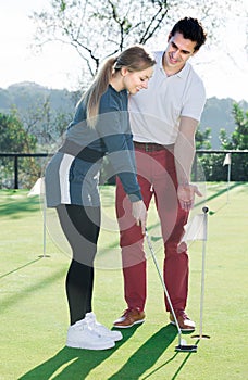 Man 30-35 years old is training woman 25-29 years old to play golf