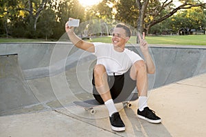 Man 30s sitting on skate board after sport boarding training session taking selfie photograph portrait or picture on mobile phone