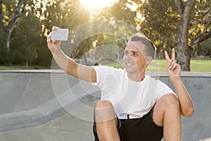 Man 30s sitting on skate board after sport boarding training session taking selfie photograph portrait or picture on mobile phone