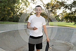 Man 30s standing holding skate board after sport boarding training session using mobile phone at half pipe track