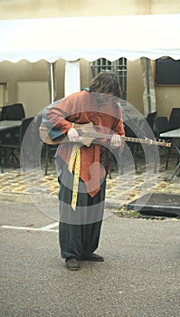 man with acoustic guitar playing on the street near tables and chairs