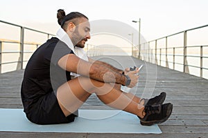 Man in activewear browsing sporty apps on phone sits outside