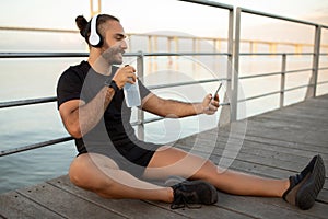 man in activewear using cellphone and earphones at sea pier