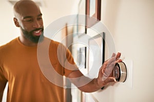 Man Adjusting Digital Central Heating Thermostat At Home