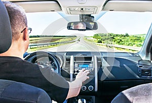 The man is adjusting sound volume in the car stereo (radio).