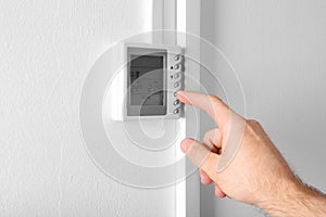 Man adjusting thermostat on white wall, closeup