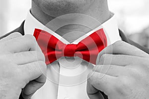 Man adjusts red bow tie with hands. Black and white photo with coloured element.