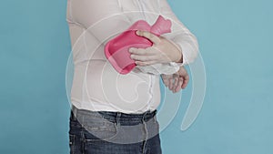 A man adjusts a red heating pad with hot water for pain in the elbow joint. Treatment of inflammation of the joints with