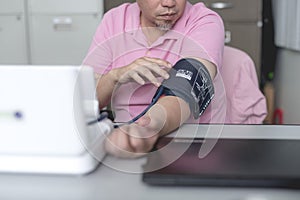 A man adjusts the velcro straps of a digital blood pressure monitor. Self checking his health at the office