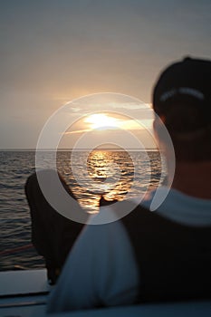 Man admiring a stunning sunset over the serene ocean, with the horizon illuminated by the sunset