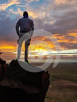 A man admiring a sunrise from a small hill in the suburbs of Xilinhot, Inner Mongolia. The sky is painted in orange, red
