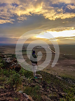 A man admiring a sunrise from a small hill in the suburbs of Xilinhot, Inner Mongolia. The sky is painted in orange, red