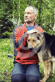 Man adventurer with big dog is resting in the forest