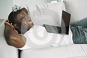 man of african appearance lies on the couch with a laptop communication leisure