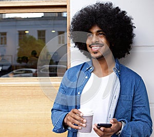 Man with afro standing outside with mobile phone ad coffee