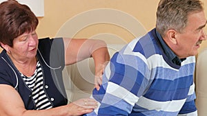 Man aged tries to get up from the couch and there is a sharp pain in his back. Wife husband massages the lower back and