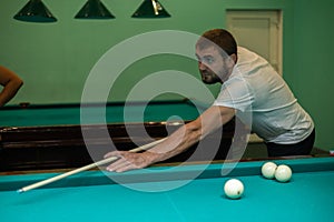 A man aims a cue at a billiard ball on a green table. A man hits a billiard ball and tries to pocket it. A man plays