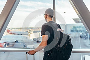 Man in airport near gate windows at planes on runway.